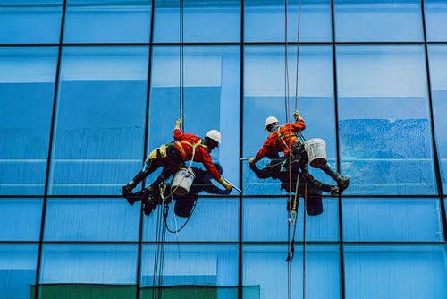 Three professional window washers from 5dmaplus company in safety harnesses cleaning the exterior of a blue glass skyscraper